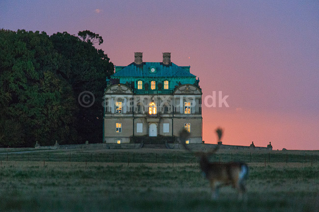 Eremitage Slottet. Solnedgangen spejler sig i vinduerne i Eremitage Slottet i aftenskumring. Bag slottet ses lyset fra den opg�ende m�ne; ; J�gersborg Dyrehave / Sj�lland; ; ; ; slotte jagtslotte sev�rdigheder aftenstemning Eremitageslottet