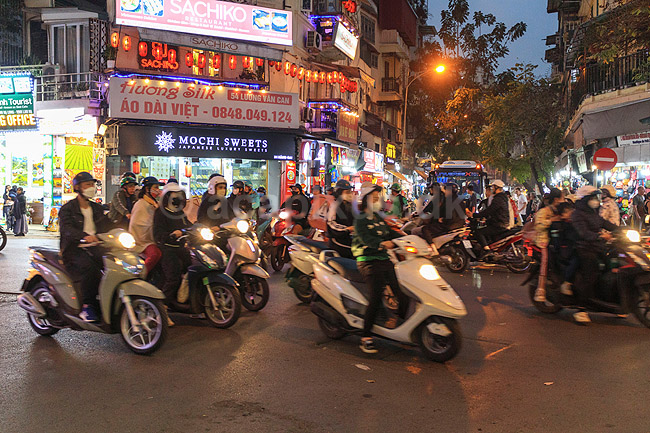 Trafik i Hanoi. Scootere fletter ind og ud imellem hinanden i Hanoi uden at nogen stopper eller tager hensyn til lysreguleringen, tilsyneladende kaotisk, men det virker meget effektivt ; ; Hanoi; Vietnam; ; ; Trafik, scootere, kaos